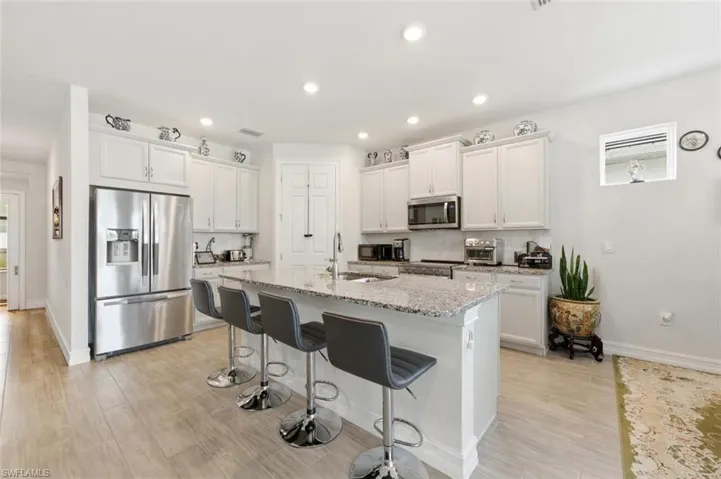 Kitchen featuring stainless steel appliances, white cabinetry, light stone countertops, a breakfast bar area, and light wood-style floors
