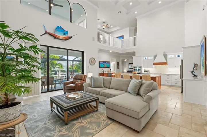 Living area featuring ceiling fan, a high ceiling, stone tile flooring, beamed ceiling, and recessed lighting