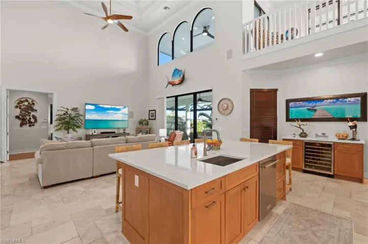 Kitchen with beverage cooler, a sink, stone tile floors, a high ceiling, and a ceiling fan