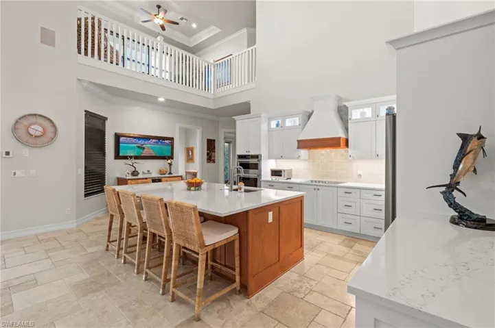 Kitchen featuring premium range hood, a towering ceiling, stone tile floors, a ceiling fan, and a breakfast bar