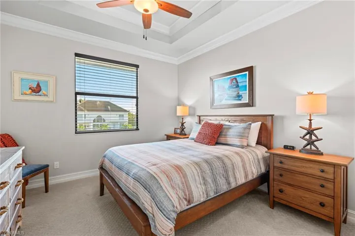 Bedroom featuring light colored carpet, a tray ceiling, crown molding, baseboards, and ceiling fan