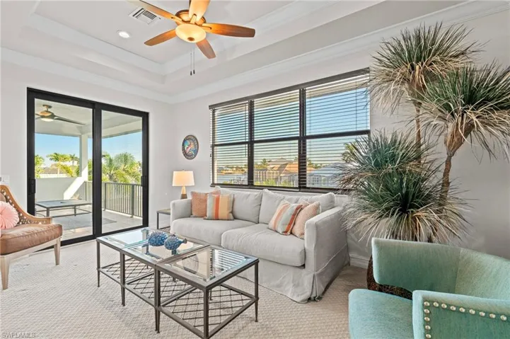 Carpeted living room featuring ceiling fan, plenty of natural light, ornamental molding, and a raised ceiling