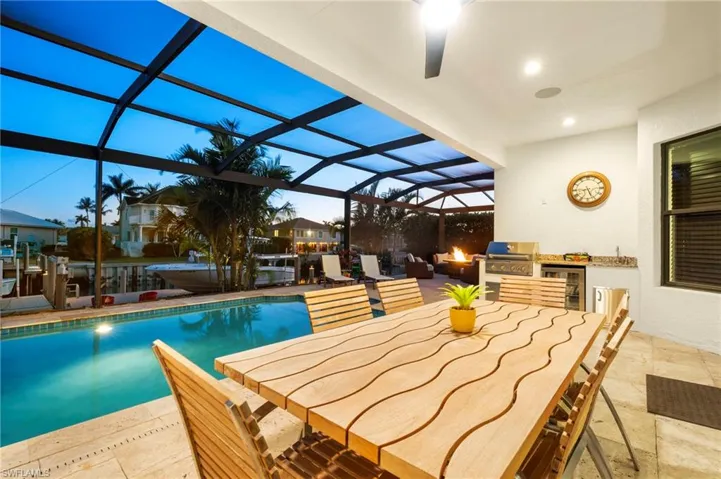 Outdoor pool featuring exterior kitchen, a patio, glass enclosure, area for grilling, and outdoor dining area