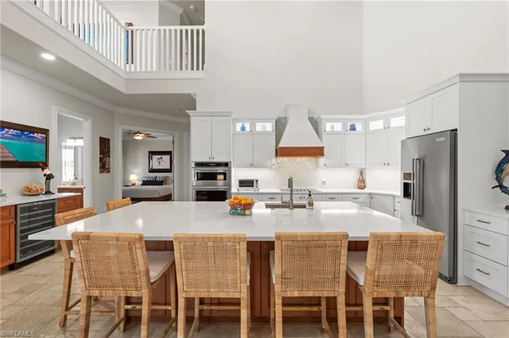 Kitchen featuring a high ceiling, appliances with stainless steel finishes, beverage cooler, custom exhaust hood, and stone tile floors