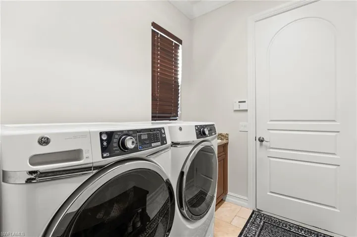 Laundry area with washing machine and dryer, light tile patterned floors, and crown molding