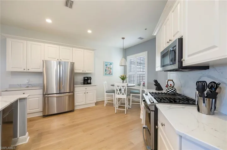 Kitchen with stainless steel appliances, white cabinetry, decorative light fixtures, light stone countertops, and recessed lighting