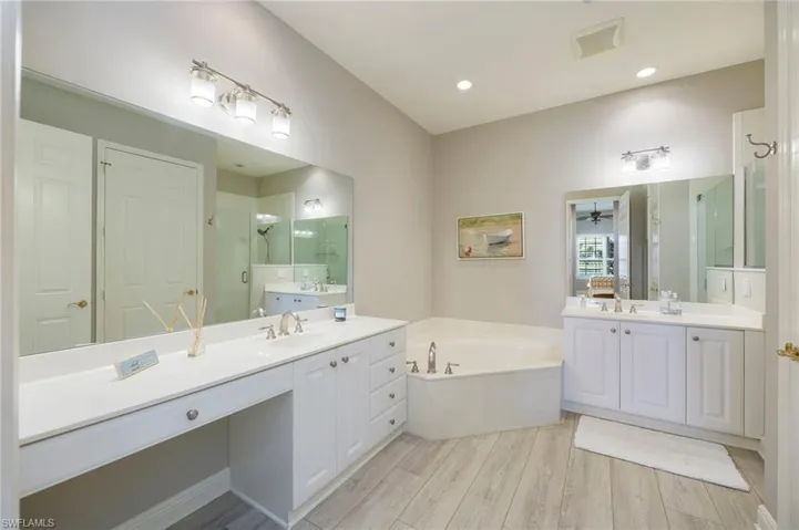 Bathroom with a stall shower, a bath, two vanities, light wood-type flooring, and ceiling fan