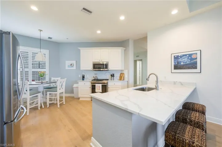Kitchen with stainless steel appliances, a kitchen breakfast bar, white cabinetry, hanging light fixtures, and a peninsula