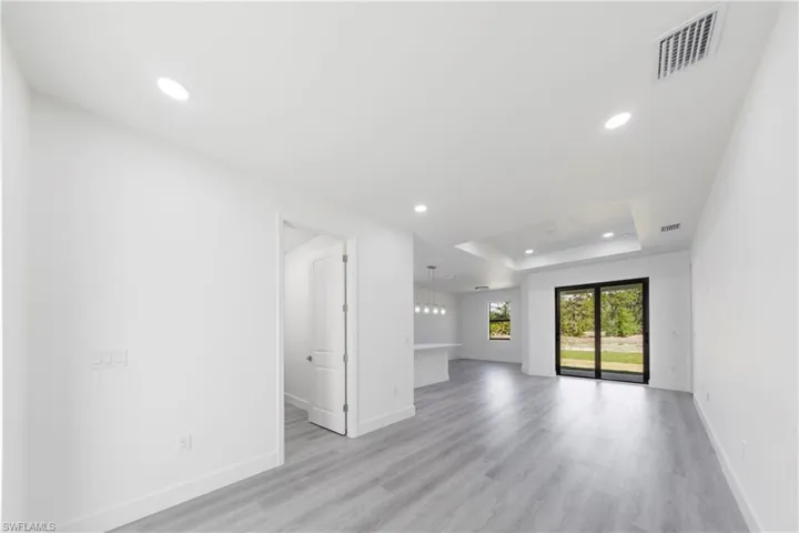 Unfurnished living room featuring a tray ceiling, visible vents, light wood-type flooring, and recessed lighting