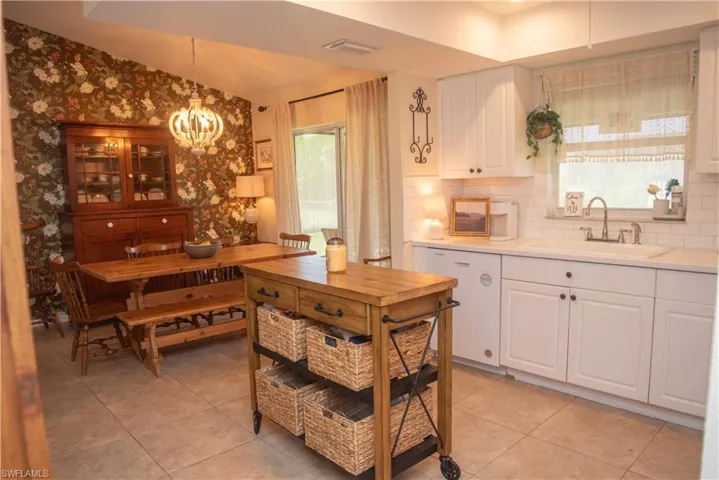 Kitchen featuring white cabinets, white dishwasher, sink, hanging light fixtures, and decorative backsplash