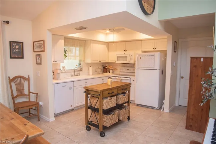 Kitchen with white appliances, light tile patterned floors, white cabinets, ceiling fan, and sink