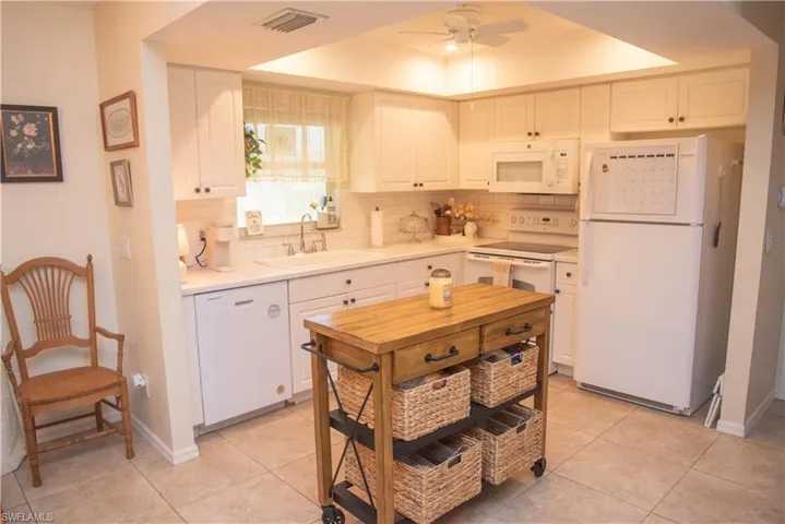 Kitchen with white appliances, sink, ceiling fan, white cabinetry, and a tray ceiling