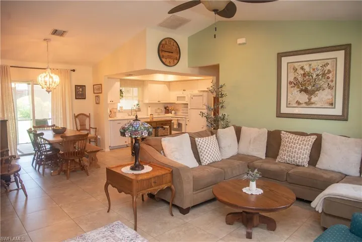 Tiled living room with sink, ceiling fan with notable chandelier, and lofted ceiling