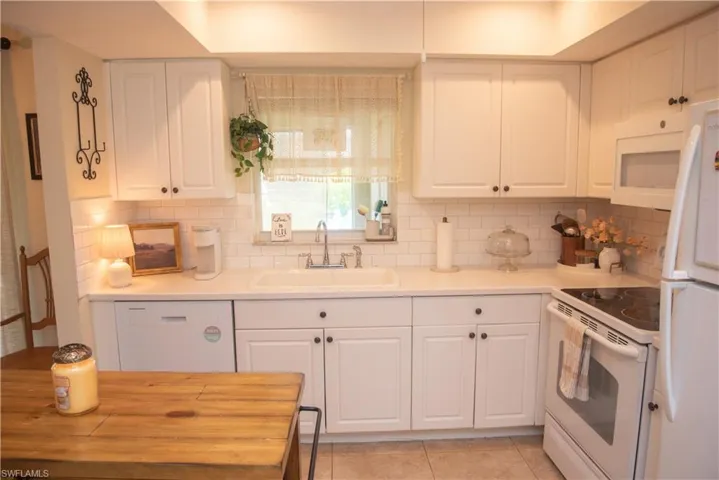 Kitchen with white cabinetry, backsplash, white appliances, and sink