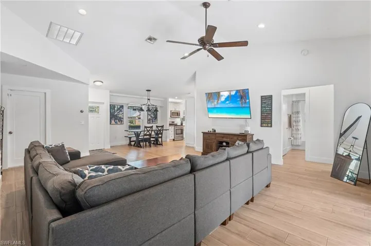 Living room with vaulted ceiling, ceiling fan, and light wood-type flooring