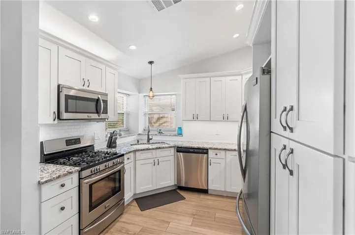 Kitchen with lofted ceiling, white cabinetry, decorative light fixtures, stainless steel appliances, and light stone countertops