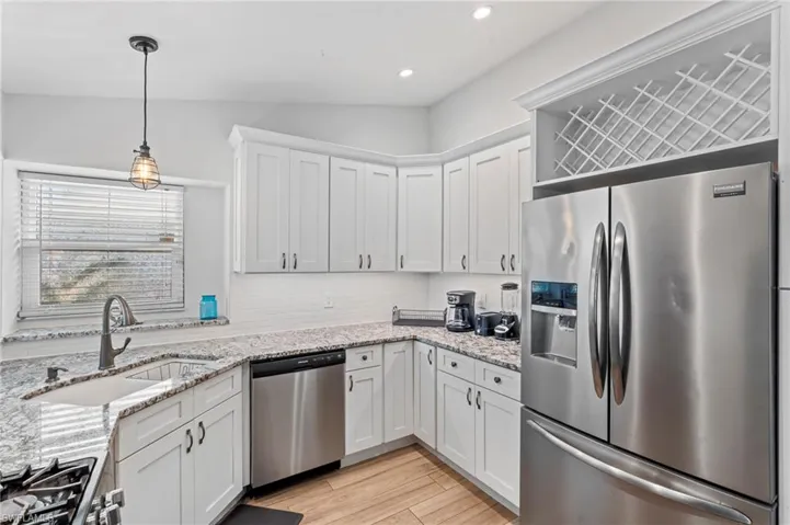 Kitchen with pendant lighting, sink, white cabinetry, backsplash, and stainless steel appliances