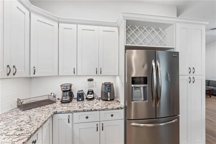 Kitchen featuring tasteful backsplash, light stone countertops, white cabinets, and stainless steel refrigerator with ice dispenser