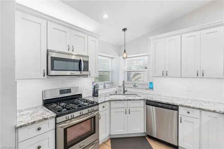 Kitchen featuring sink, white cabinetry, vaulted ceiling, appliances with stainless steel finishes, and pendant lighting