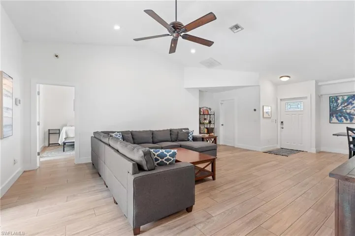 Living room featuring lofted ceiling, ceiling fan, and light wood-type flooring