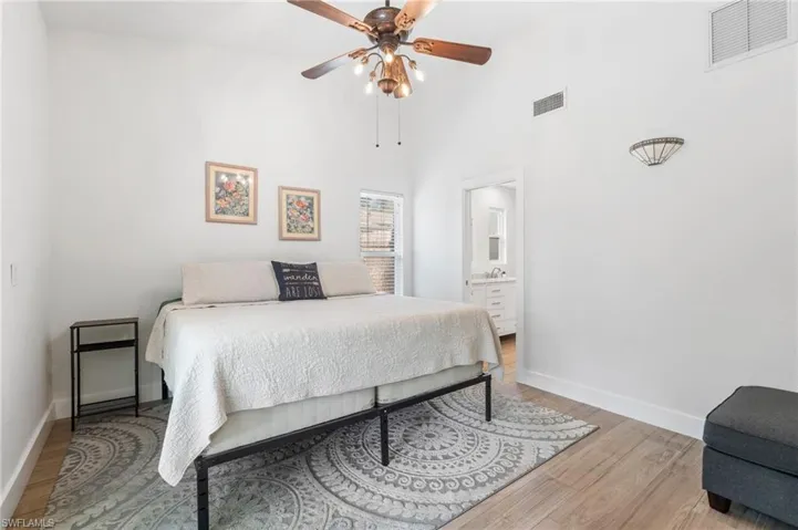Bedroom with a towering ceiling, connected bathroom, ceiling fan, and light hardwood / wood-style flooring