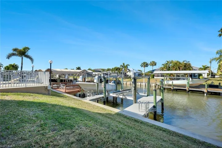 Dock featuring a water view, boat lift, a lawn, and a residential view