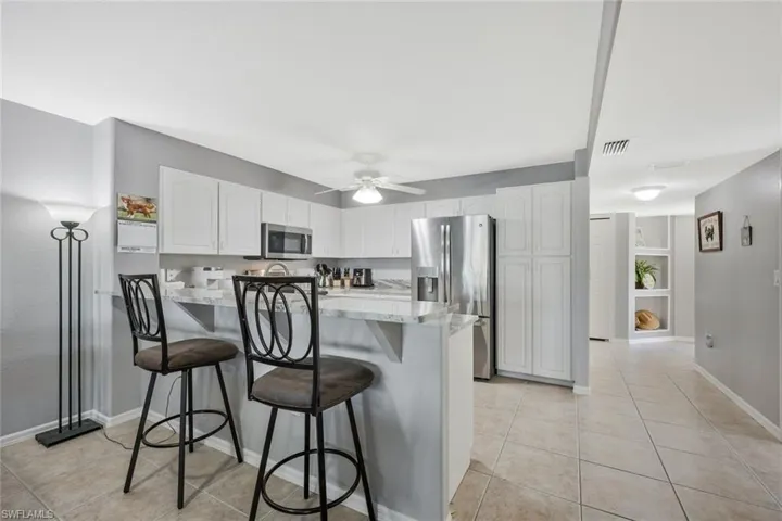 Kitchen with a peninsula, stainless steel appliances, light stone counters, and light tile patterned floors
