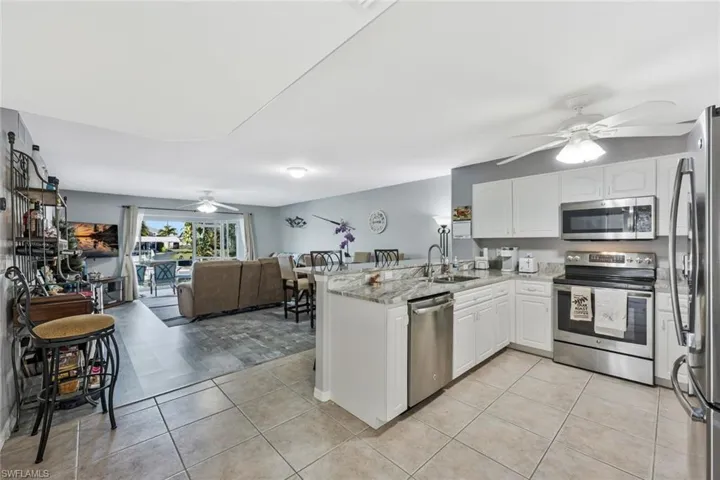Kitchen featuring a ceiling fan, stainless steel appliances, open floor plan, white cabinets, and a peninsula