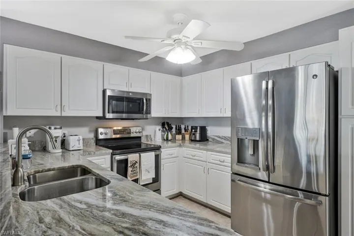 Kitchen featuring stainless steel appliances, light stone countertops, white cabinets, and ceiling fan