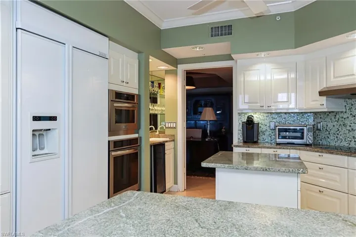 Kitchen with tasteful backsplash, paneled refrigerator, black electric cooktop, ornamental molding, and white cabinets