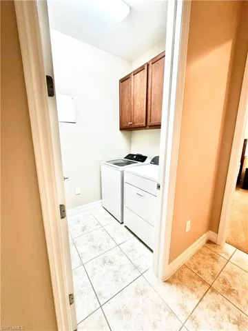 Washroom with cabinet space, light tile patterned floors, and washer and dryer