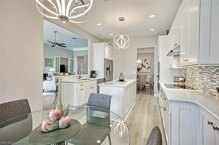 Kitchen featuring appliances with stainless steel finishes, white cabinetry, ceiling fan with notable chandelier, pendant lighting, and a center island