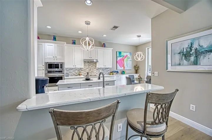 Kitchen with white cabinetry, kitchen peninsula, hanging light fixtures, backsplash, and appliances with stainless steel finishes