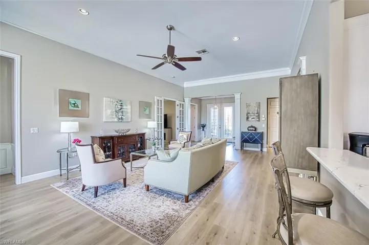 Living room with ornamental molding, light wood-type flooring, ceiling fan, and french doors