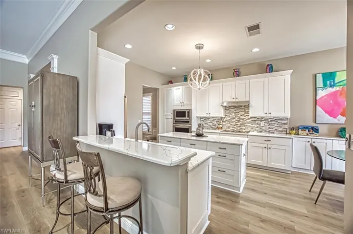 Kitchen featuring an island with sink, appliances with stainless steel finishes, hanging light fixtures, and white cabinetry