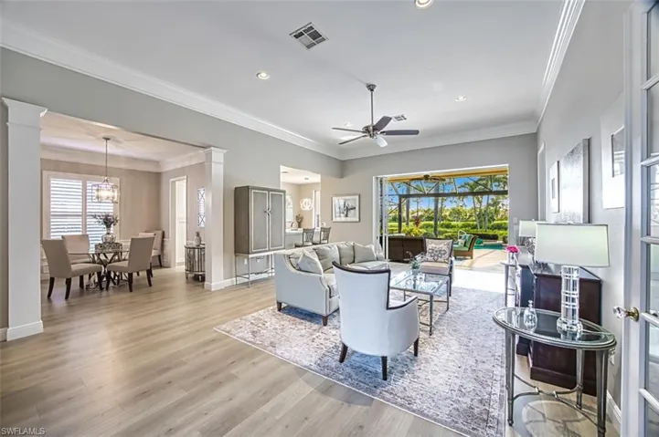 Living room with light wood-type flooring, ceiling fan with notable chandelier, ornamental molding, and a wealth of natural light