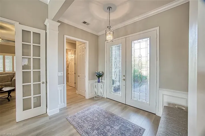 Foyer entrance featuring light wood-type flooring, decorative columns, french doors, and crown molding