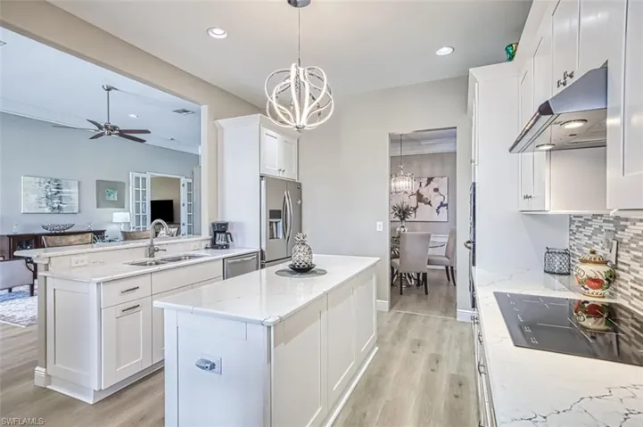 Kitchen with appliances with stainless steel finishes, ceiling fan with notable chandelier, a kitchen island, and white cabinetry