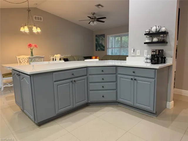 Kitchen with visible vents, gray cabinetry, vaulted ceiling, and ceiling fan with notable chandelier