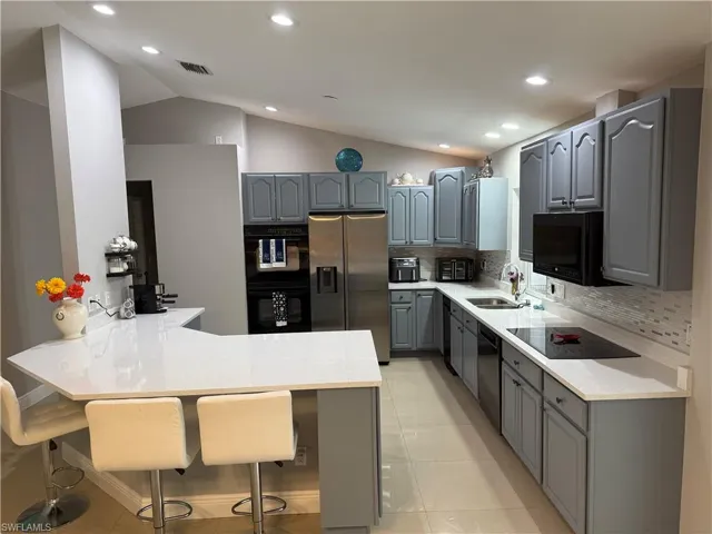 Kitchen featuring gray cabinets, a peninsula, a sink, and black appliances