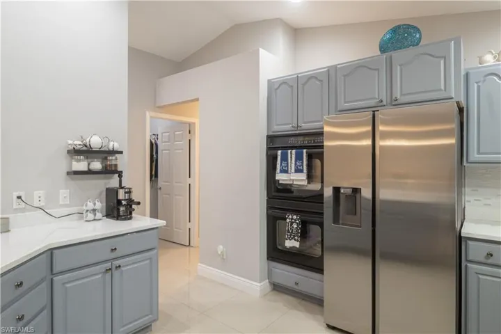 Kitchen featuring stainless steel fridge with ice dispenser, gray cabinetry, vaulted ceiling, light tile patterned floors, and baseboards