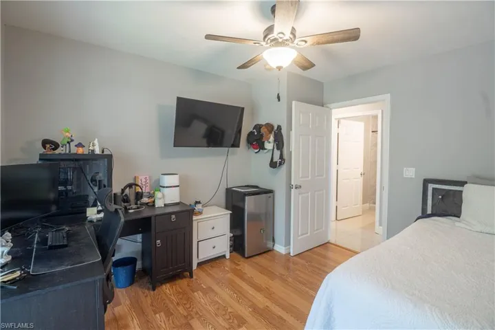 Bedroom with light wood-type flooring, an office area, fridge, and a ceiling fan