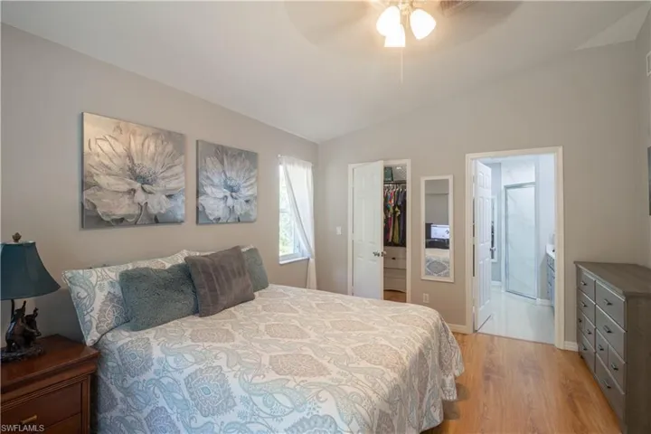 Bedroom with light wood finished floors, lofted ceiling, a walk in closet, a closet, and ensuite bath