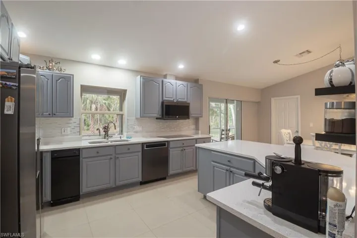 Kitchen featuring gray cabinetry, a sink, stainless steel appliances, tasteful backsplash, and lofted ceiling