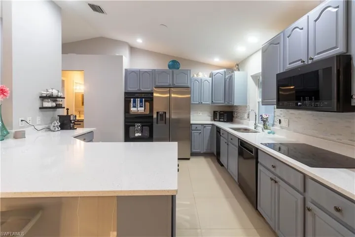 Kitchen featuring black appliances, a sink, gray cabinetry, vaulted ceiling, and decorative backsplash