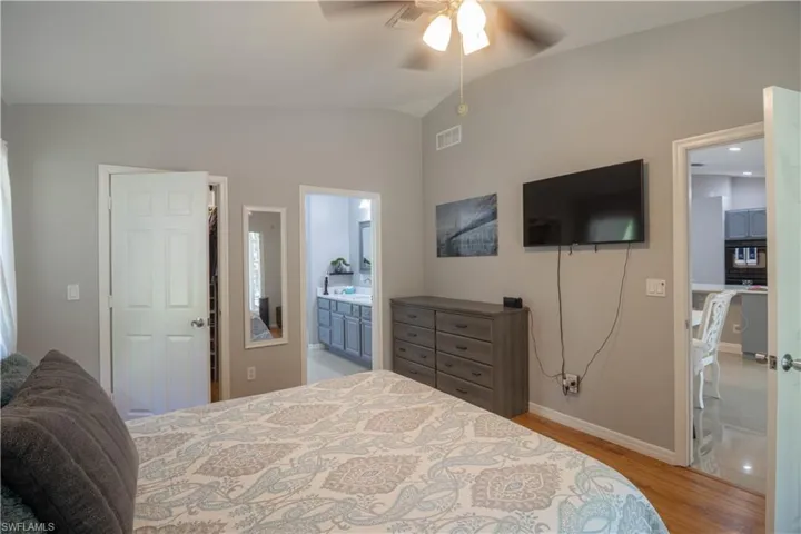 Bedroom featuring vaulted ceiling, light wood-style flooring, baseboards, ensuite bathroom, and a ceiling fan