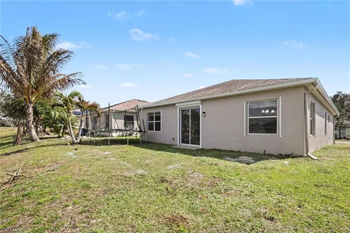 Rear view of property featuring stucco siding, a trampoline, and a lawn