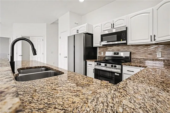 Kitchen featuring light stone counters, stainless steel appliances, white cabinetry, and decorative backsplash