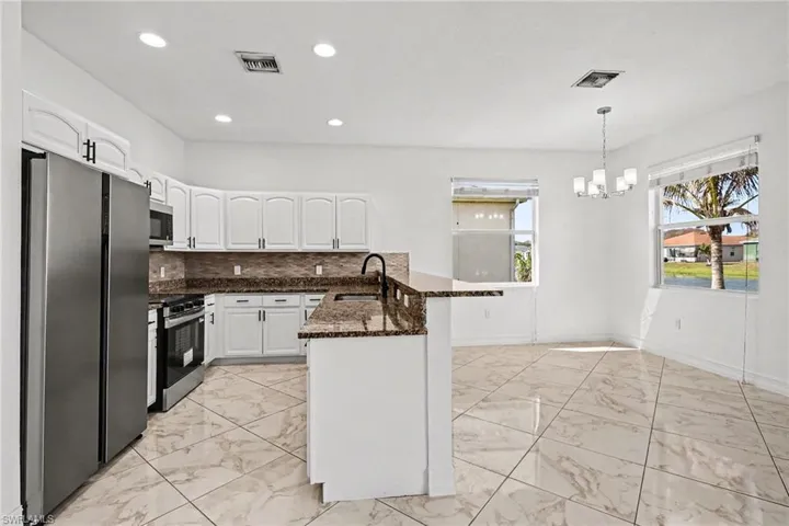 Kitchen with a peninsula, stainless steel appliances, dark stone counters, white cabinets, and light marble finish flooring
