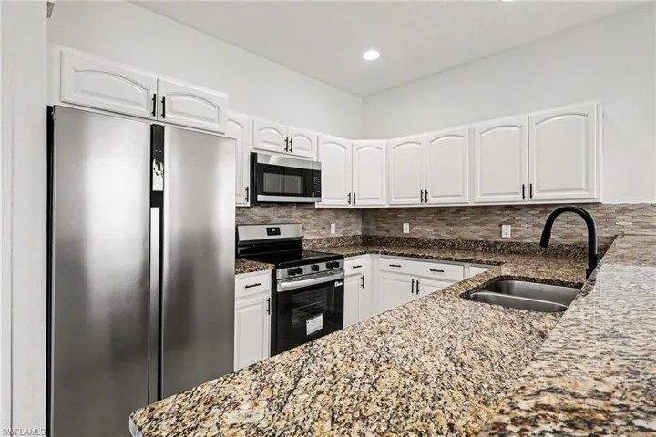 Kitchen featuring stainless steel appliances, dark stone counters, decorative backsplash, white cabinetry, and recessed lighting